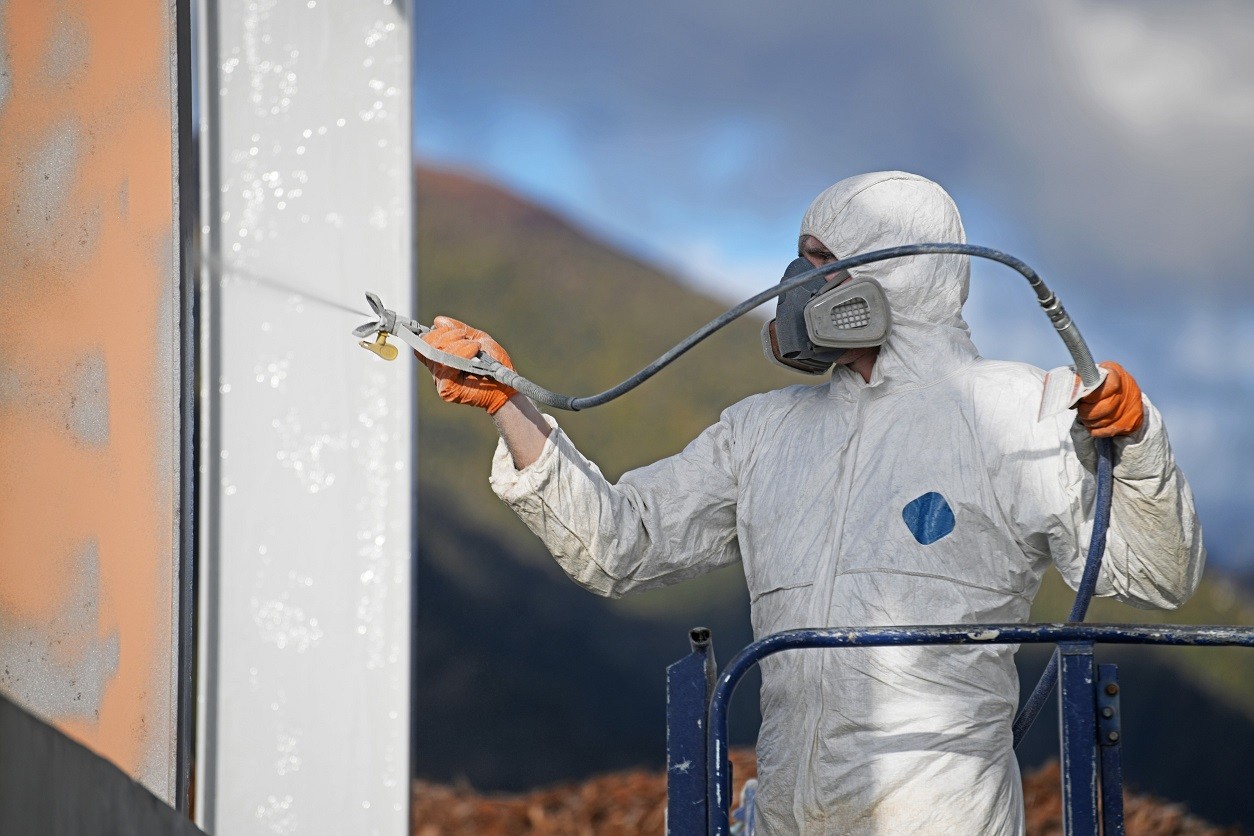 Specjalista malujący elewację w pełnym kombinezonie malarskim